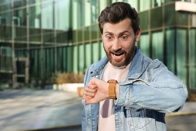 Photo of Emotional man checking time on watch near building. Being late concept