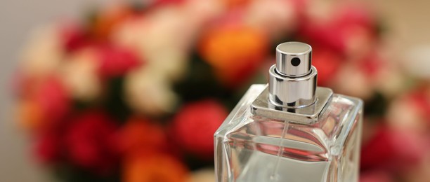 Photo of Bottle of perfume against beautiful roses, closeup and space for text. Banner design