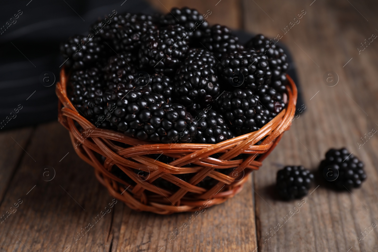 Photo of Fresh ripe blackberries in wicker bowl on wooden table, closeup