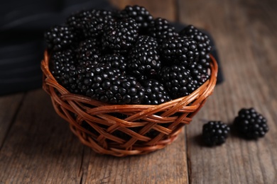 Photo of Fresh ripe blackberries in wicker bowl on wooden table, closeup