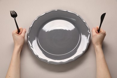 Photo of Woman with cutlery and empty plate at gray table, above view