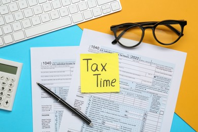 Photo of Reminder note with words Tax Time, documents, computer keyboard, calculator and glasses on color background, flat lay