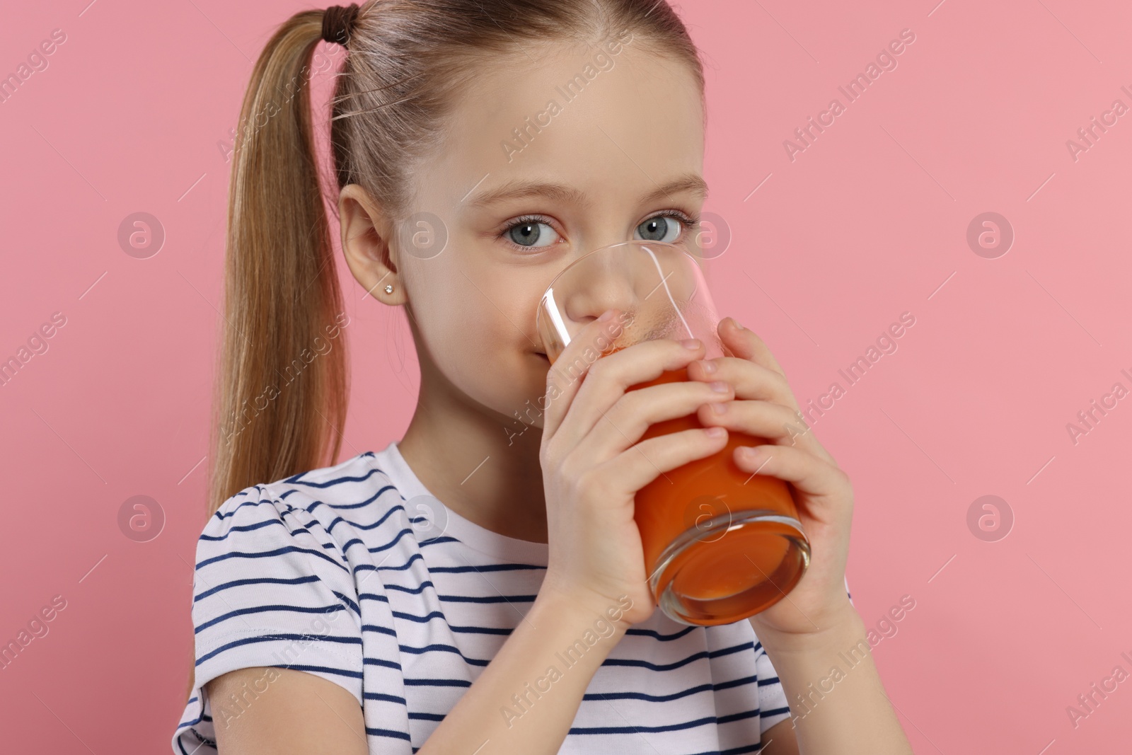 Photo of Little girl drinking fresh juice on pink background