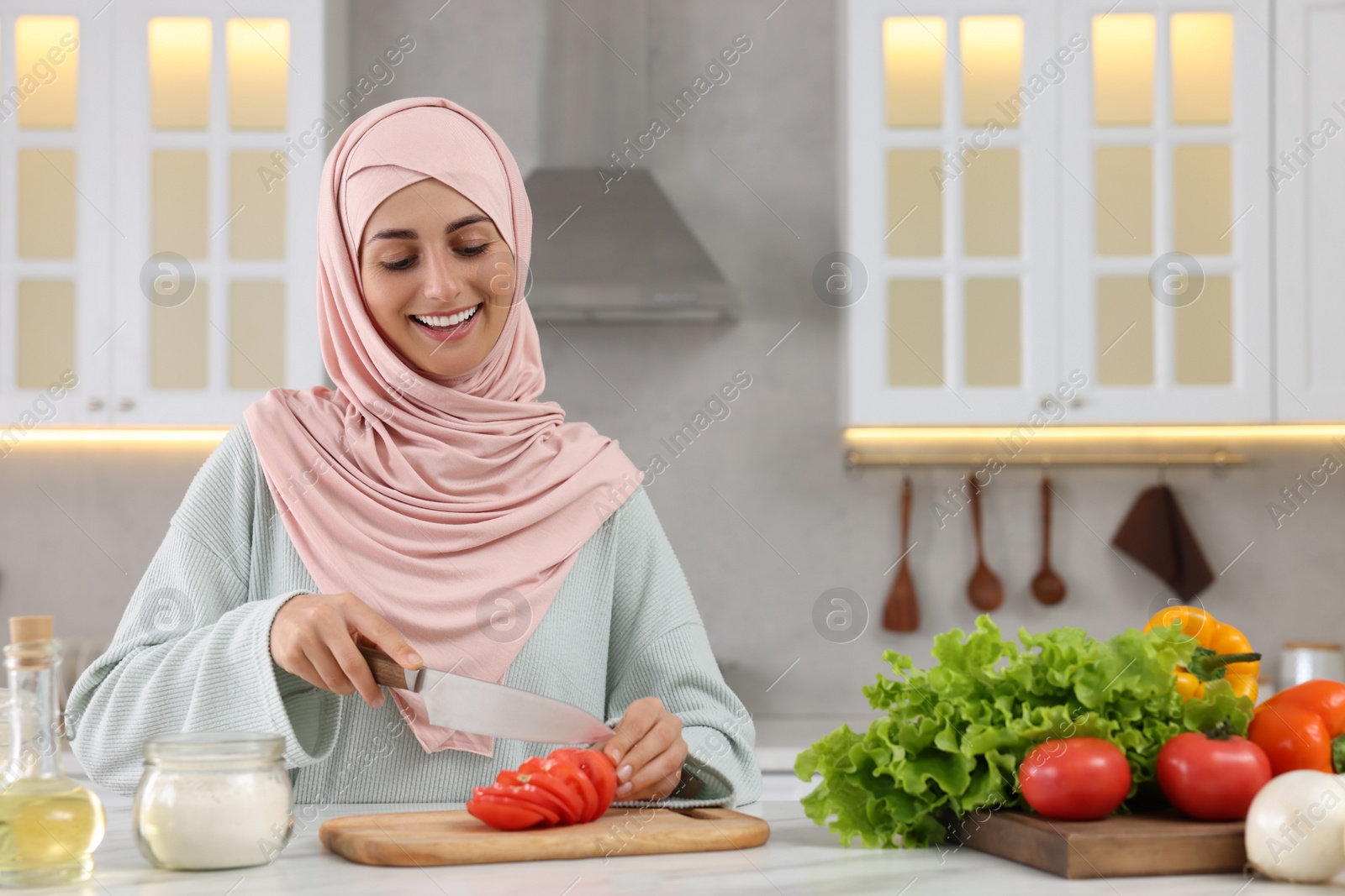 Photo of Muslim woman making delicious salad with vegetables at white table in kitchen. Space for text