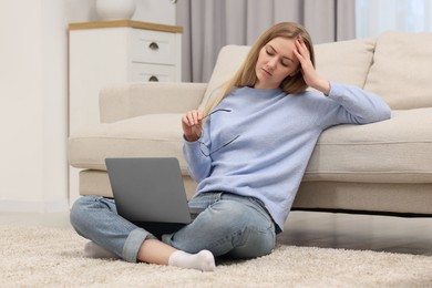 Overwhelmed young woman sitting with laptop on floor at home