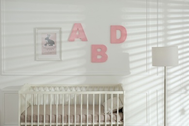Photo of Comfortable crib near wall with pink letters in baby room. Interior design