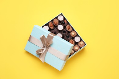 Photo of Open box of delicious chocolate candies on yellow background, flat lay