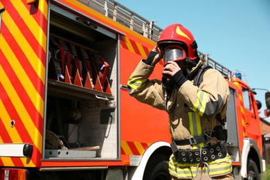 Photo of Firefighter in uniform wearing helmet and mask near fire truck outdoors, low angle view