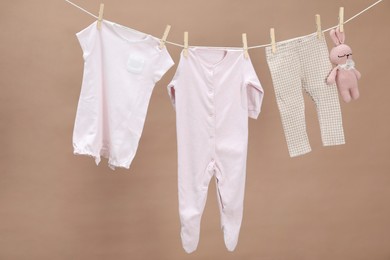 Photo of Different baby clothes and bunny toy drying on laundry line against light brown background