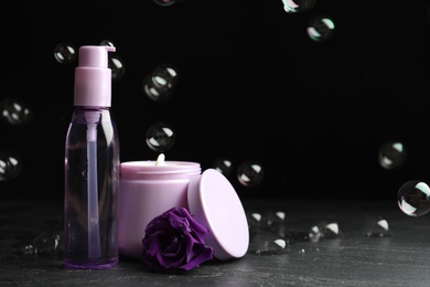Photo of Hair cosmetic products, flower and soap bubbles on black background. Space for text