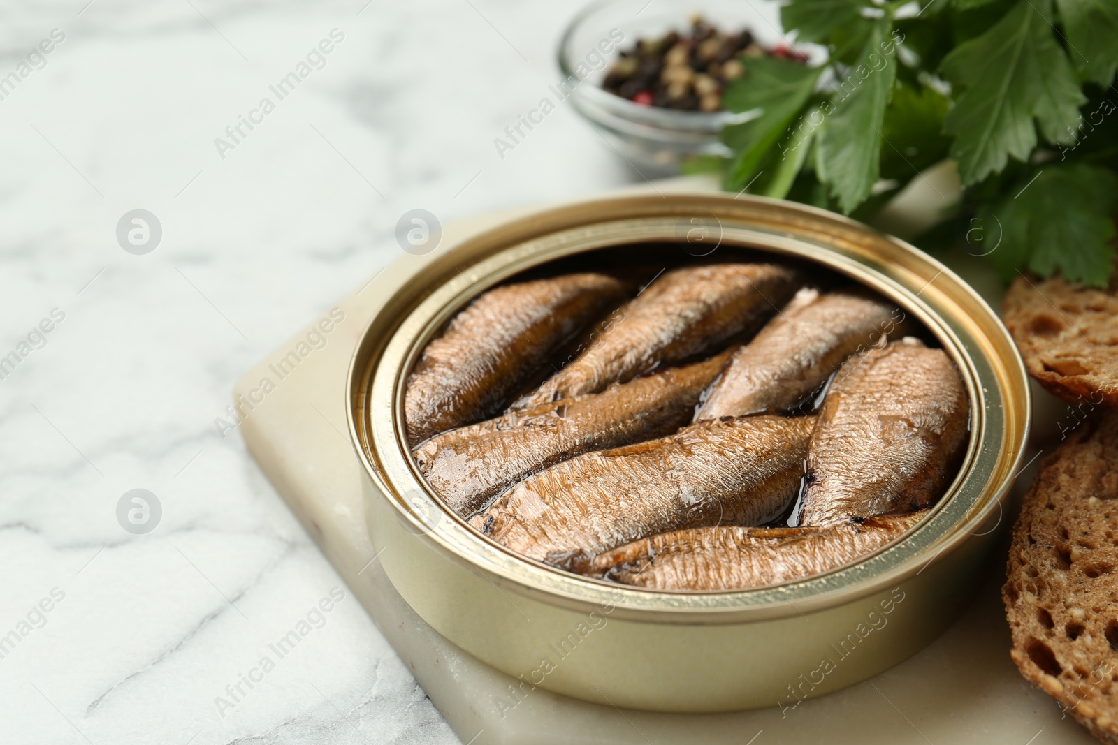 Photo of Tin can with tasty sprats served on white marble table, closeup. Space for text