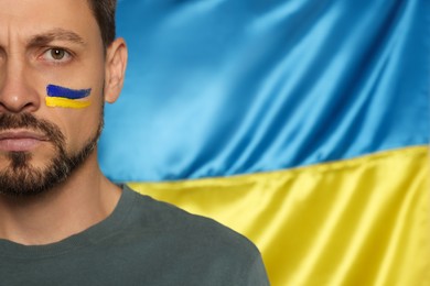 Photo of Angry man with face paint near Ukrainian flag, closeup. Space for text