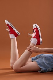 Woman wearing red classic old school sneakers on brown background, closeup