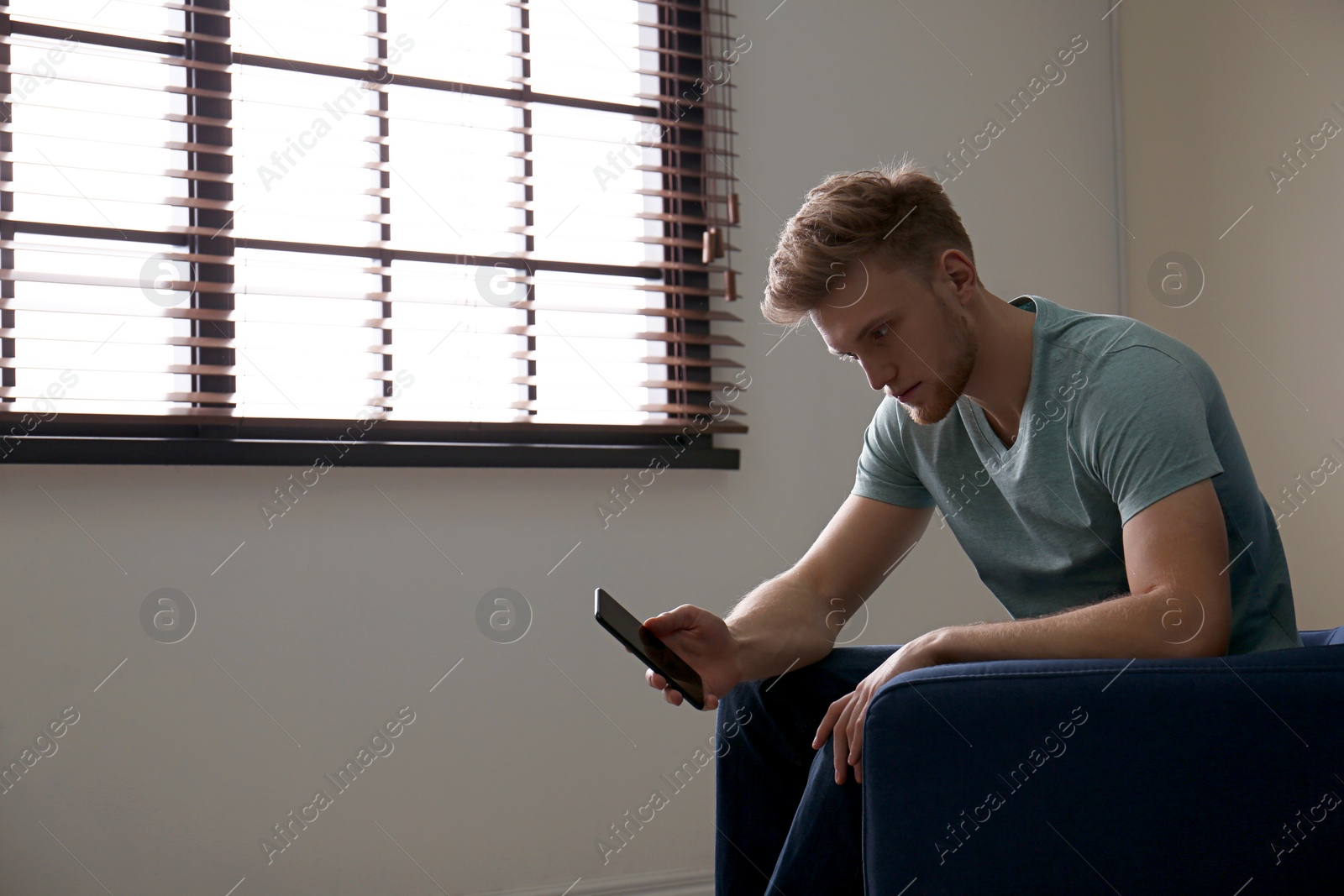 Photo of Lonely man with mobile phone in armchair near window indoors