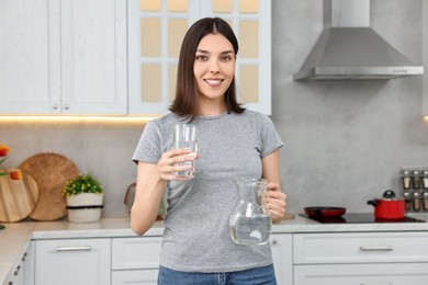 Photo of Woman with jug and glass of water in kitchen