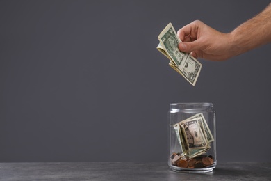 Photo of Man putting money into donation jar on table against grey background, closeup. Space for text