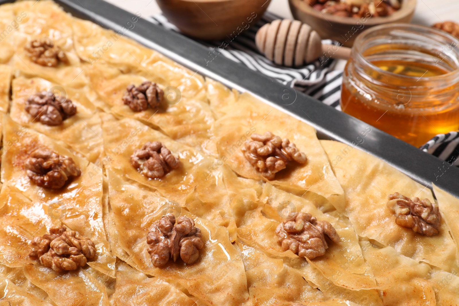 Photo of Delicious baklava with walnuts in baking pan and ingredients on table, closeup