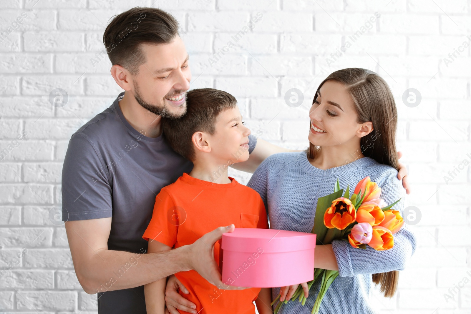 Photo of Happy woman receiving gifts from her husband and son on brick wall background. Mother's day celebration