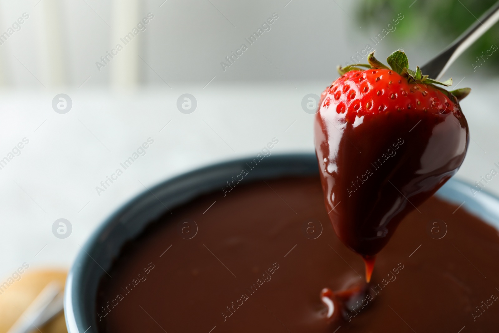 Photo of Dipping strawberry into fondue pot with chocolate, closeup. Space for text