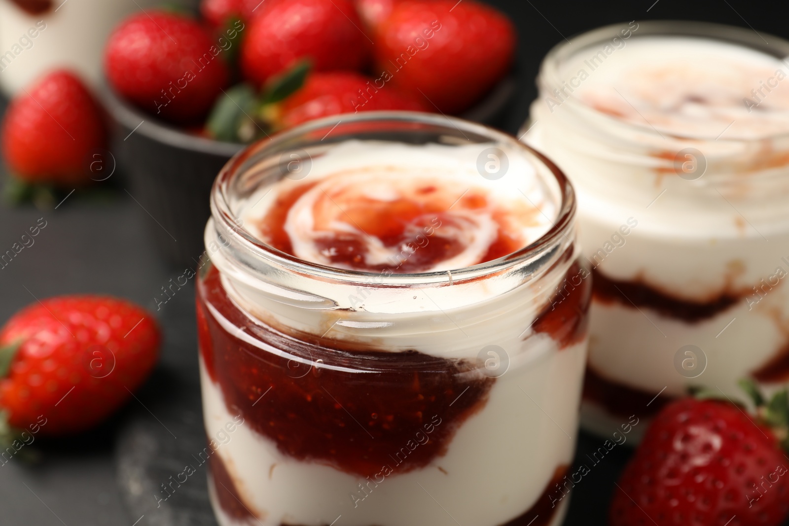 Photo of Tasty yoghurt with jam and strawberries on black table, closeup