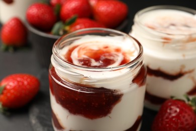 Tasty yoghurt with jam and strawberries on black table, closeup