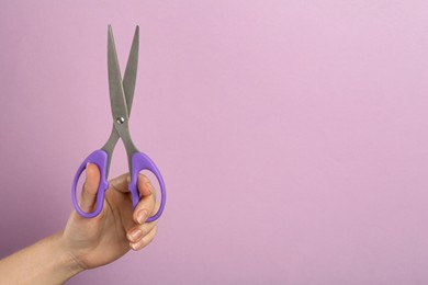 Photo of Woman holding office scissors on lilac background, closeup. Space for text