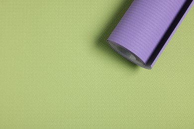 Photo of One violet wallpaper roll on green sample, top view. Space for text