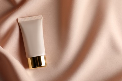 Tube of skin foundation on beige cloth, top view with space for text. Makeup product