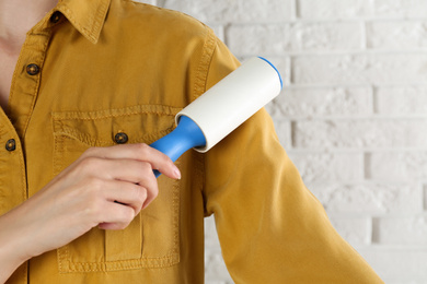 Photo of Woman cleaning yellow shirt with lint roller against white brick wall, closeup