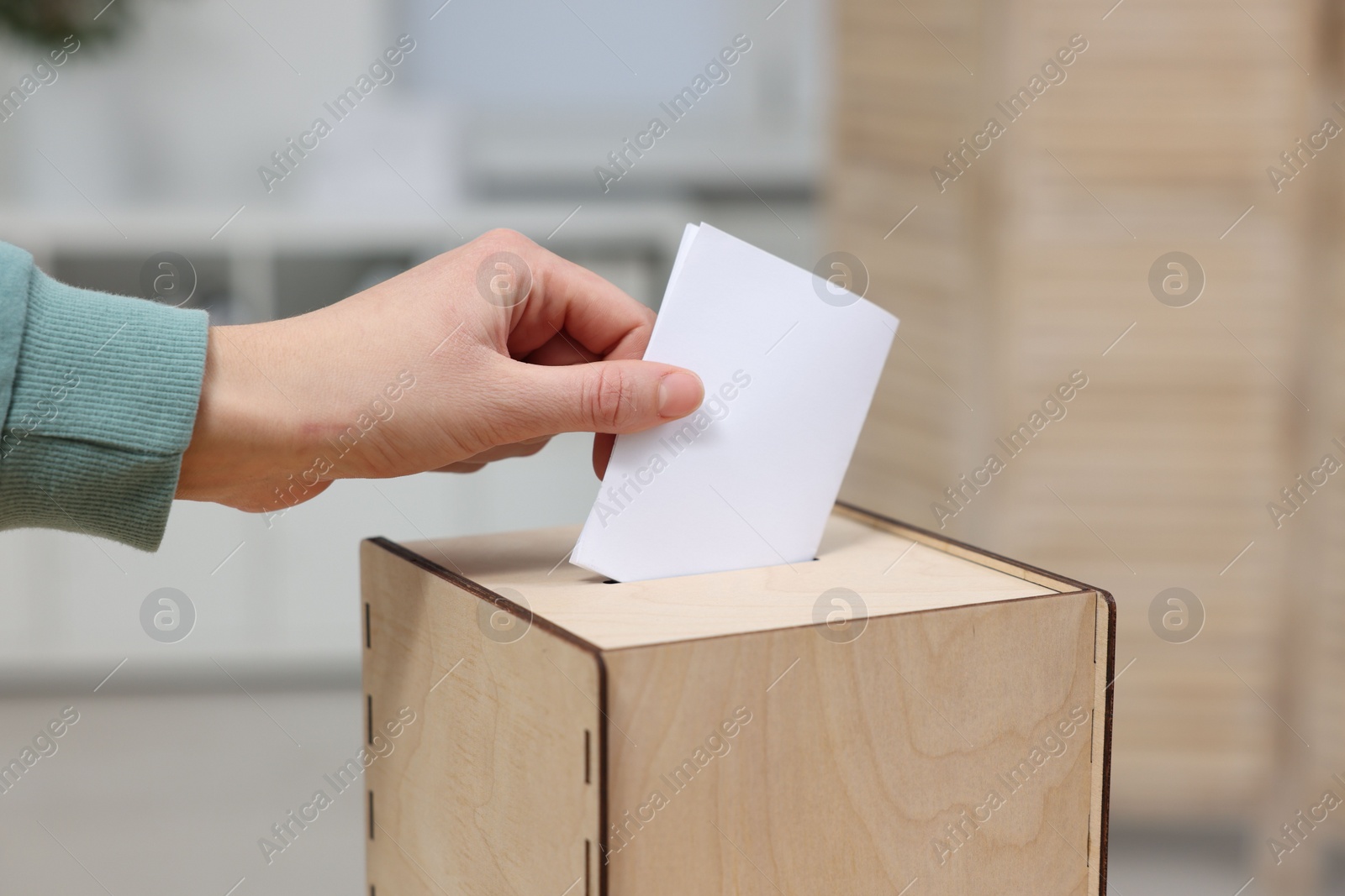 Photo of Woman putting her vote into ballot box on blurred background, closeup