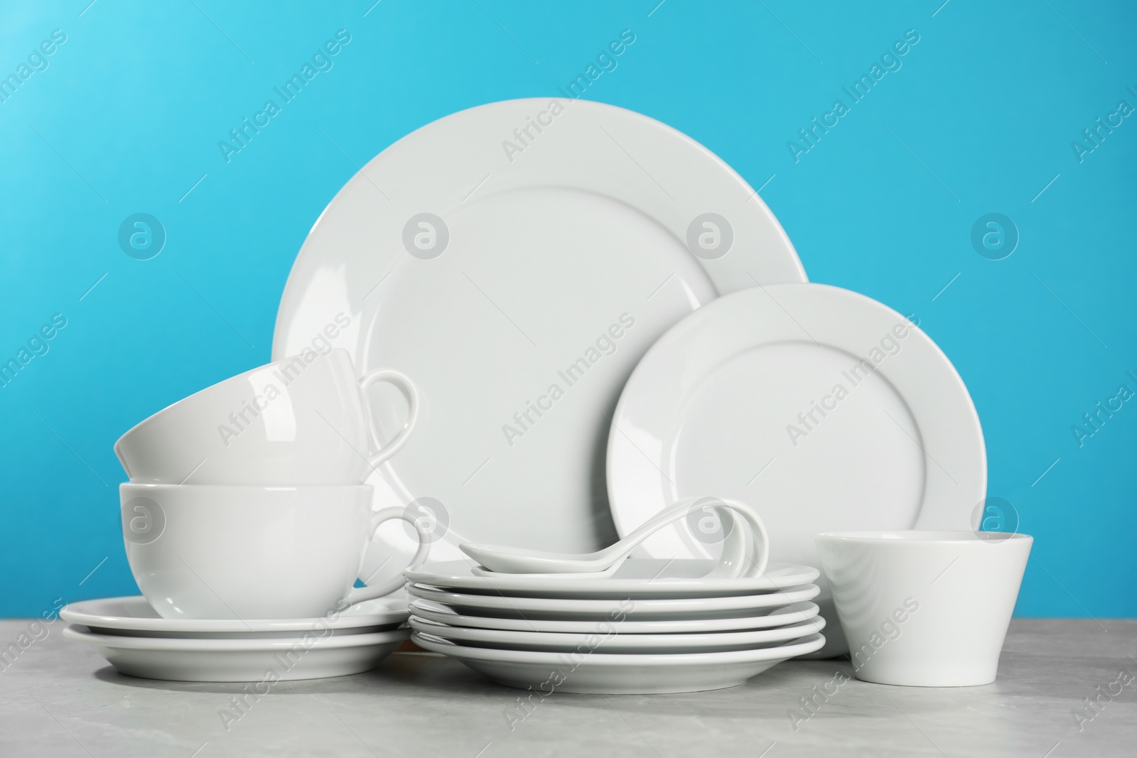 Photo of Set of clean dishware on grey table against light blue background