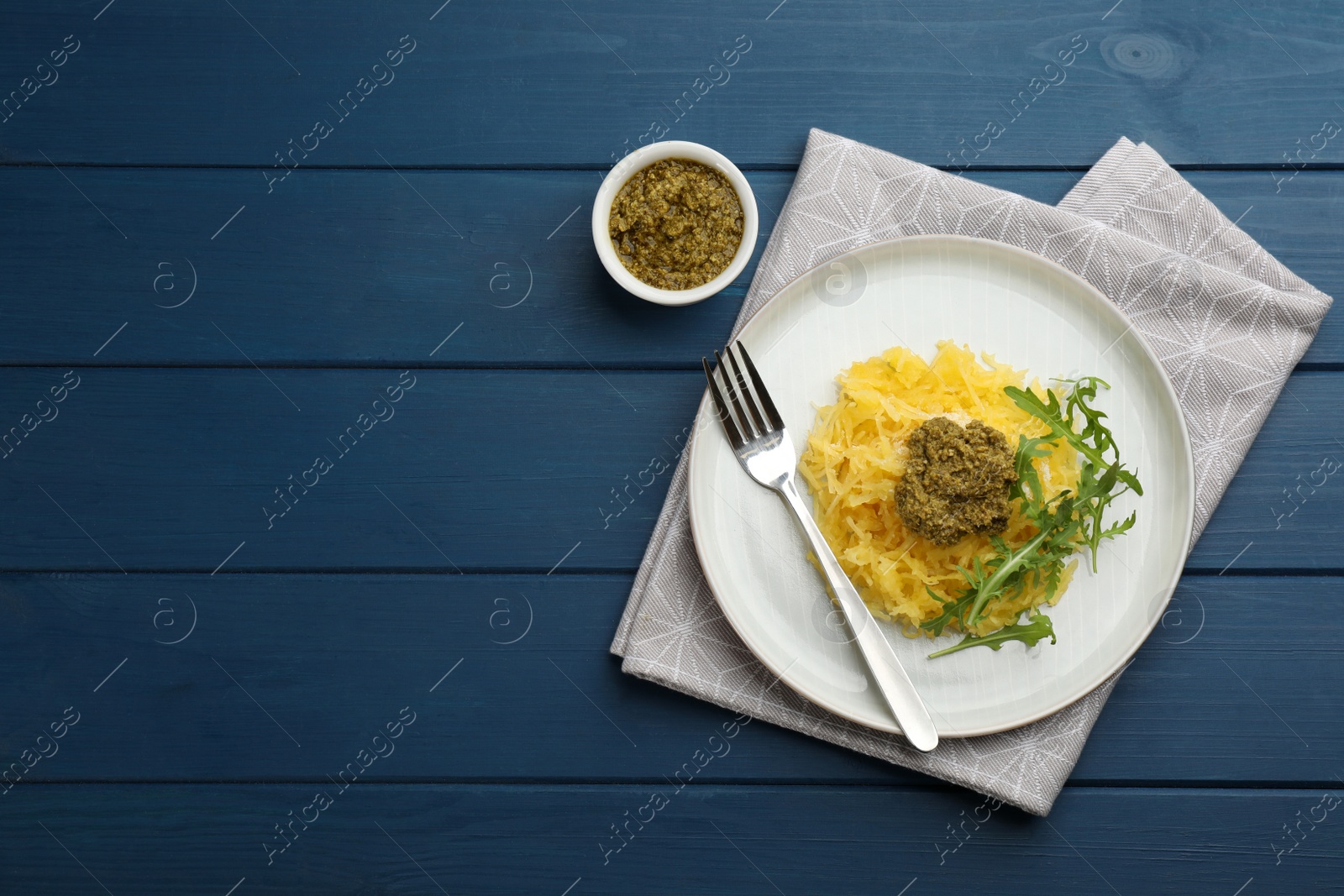 Photo of Tasty spaghetti squash with pesto sauce and arugula served on blue wooden table, flat lay. Space for text