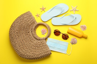 Photo of Stylish bag with beach accessories and protective mask on yellow background, flat lay