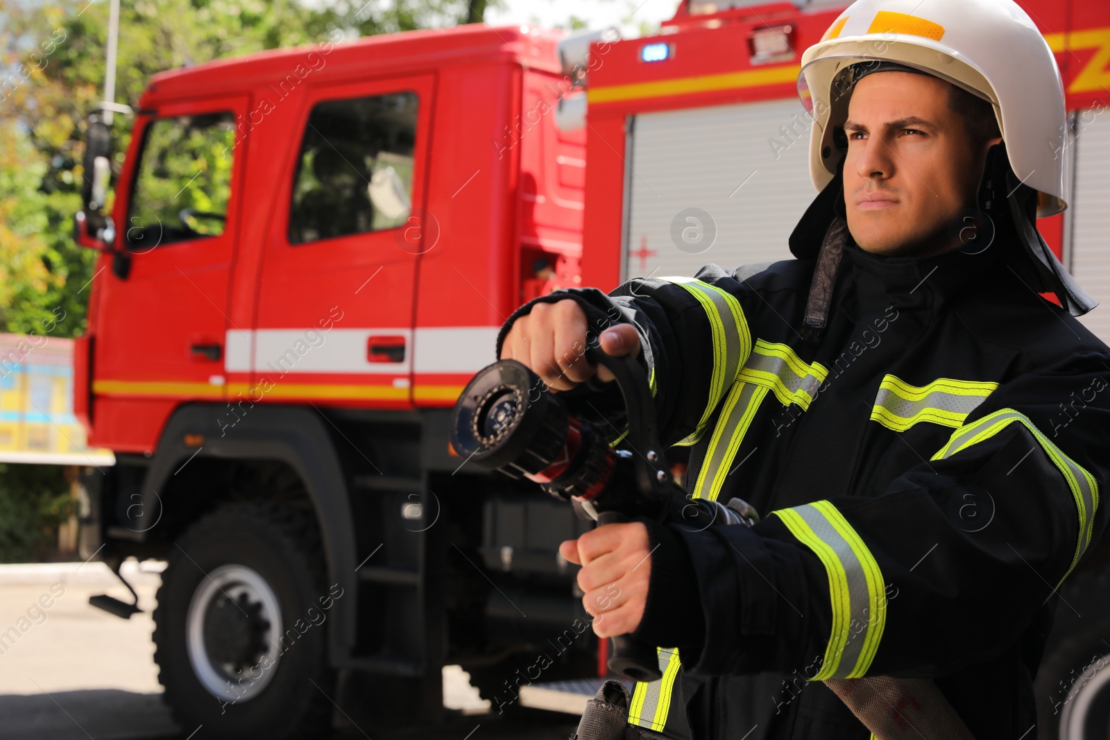 Photo of Firefighter in uniform with high pressure water jet near fire truck outdoors