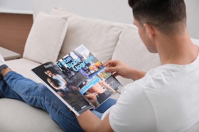 Man reading on sofa in living room, focus on magazine