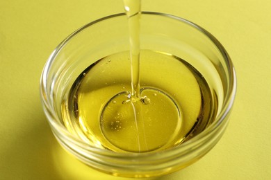 Photo of Pouring cooking oil into bowl on yellow background, closeup
