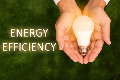 Image of Energy efficiency concept. Man holding lamp bulb against green background, top view