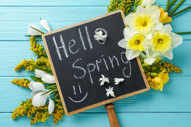 Blackboard with words HELLO SPRING and flowers on light blue wooden table, flat lay