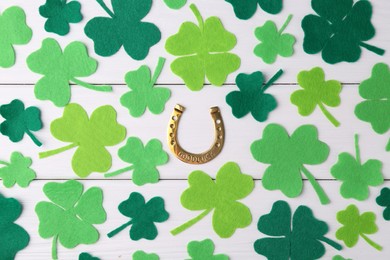 Photo of St. Patrick's day. Golden horseshoe and green decorative clover leaves on white wooden table, flat lay