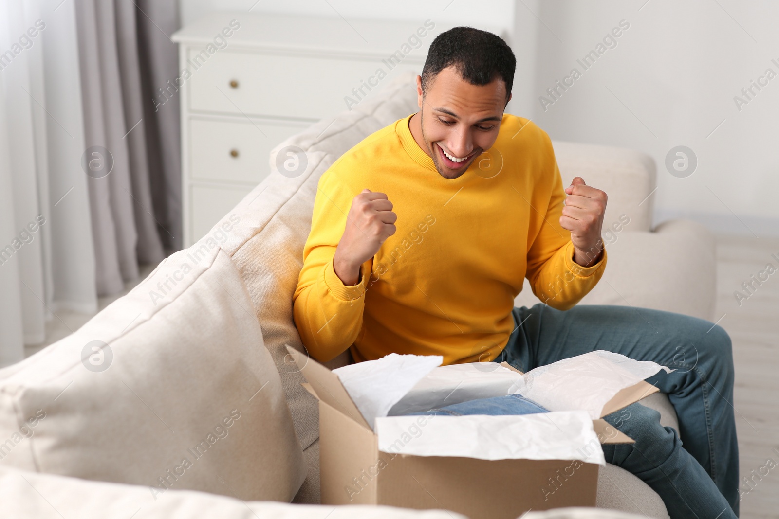 Photo of Emotional young man opening parcel at home. Internet shopping