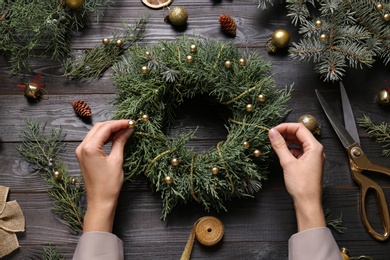 Photo of Florist making beautiful Christmas wreath at black wooden table, top view