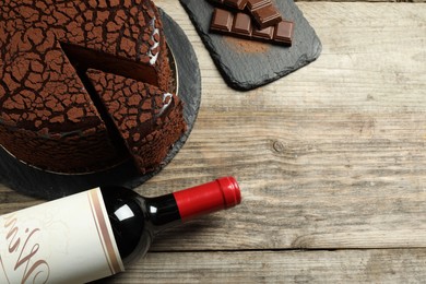 Photo of Delicious truffle cake, bottle of wine and chocolate pieces on wooden table, above view. Space for text