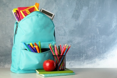 Bright backpack with school stationery on table against blue background, space for text