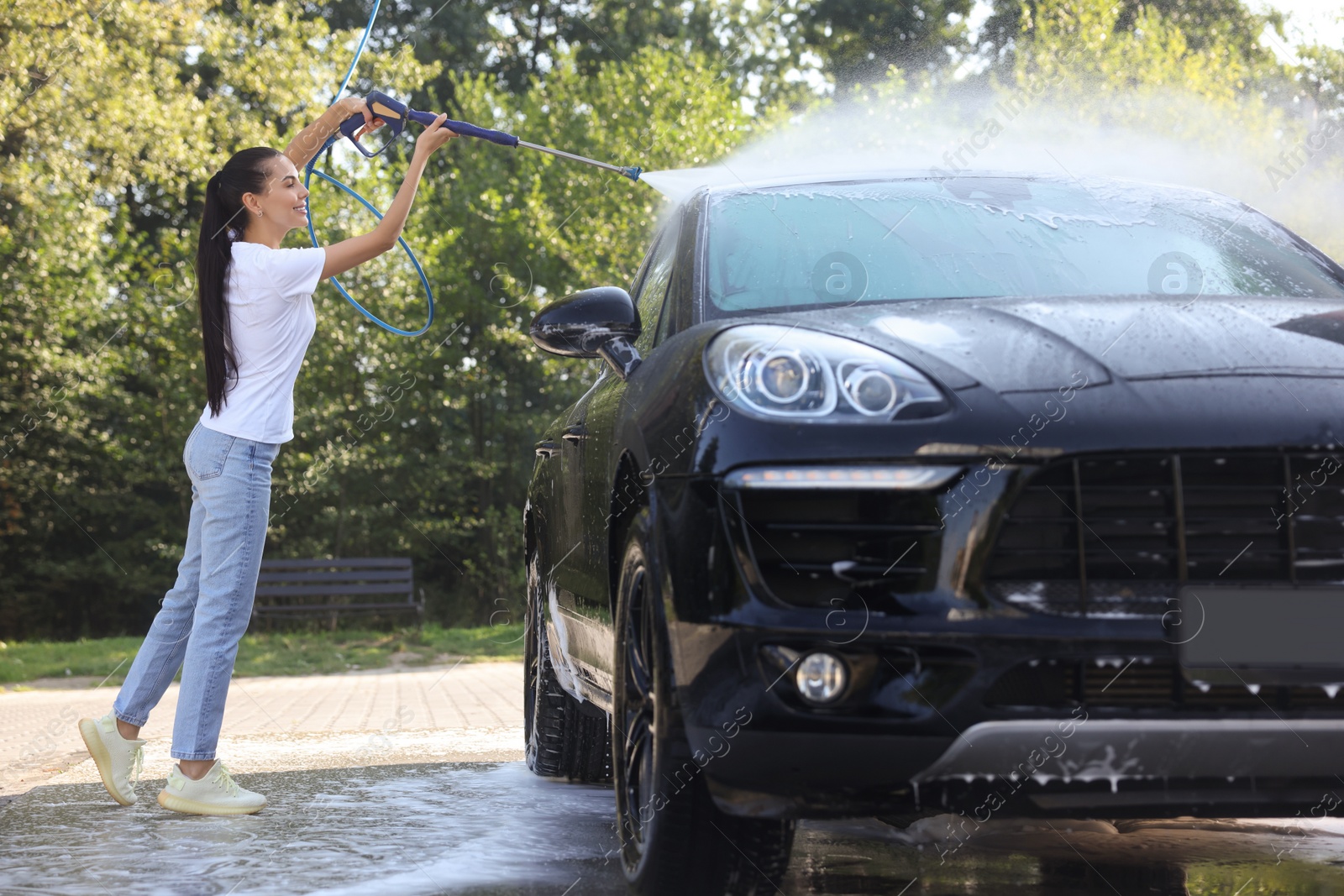 Photo of Happy woman washing car with high pressure water jet outdoors