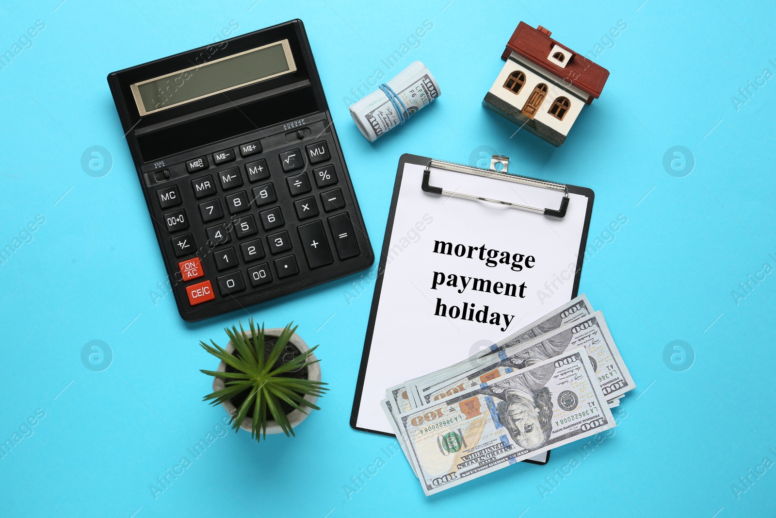 Photo of Flat lay composition of clipboard with words Mortgage Payment Holiday and house model on light blue background