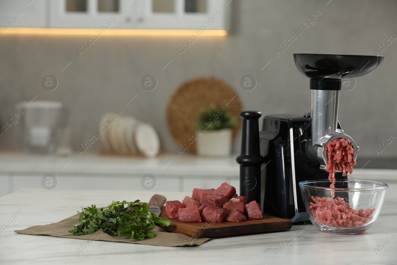 Photo of Electric meat grinder with beef mince and parsley on white table in kitchen