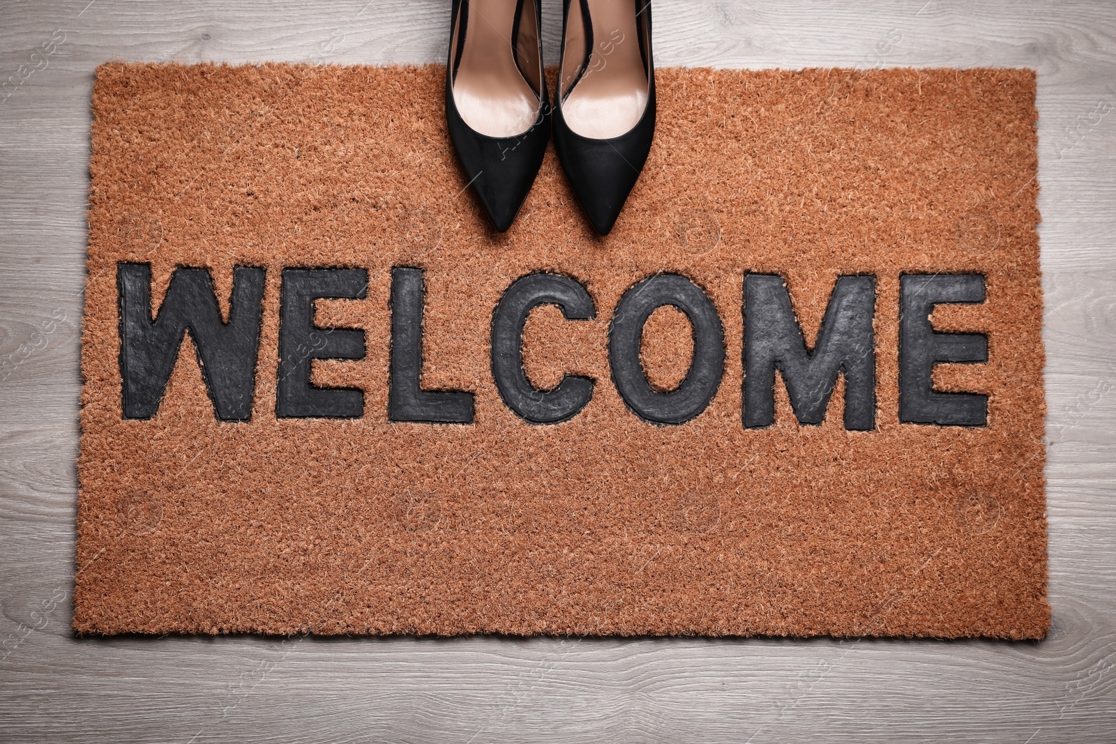 Photo of New clean mat with word WELCOME and shoes on floor, top view