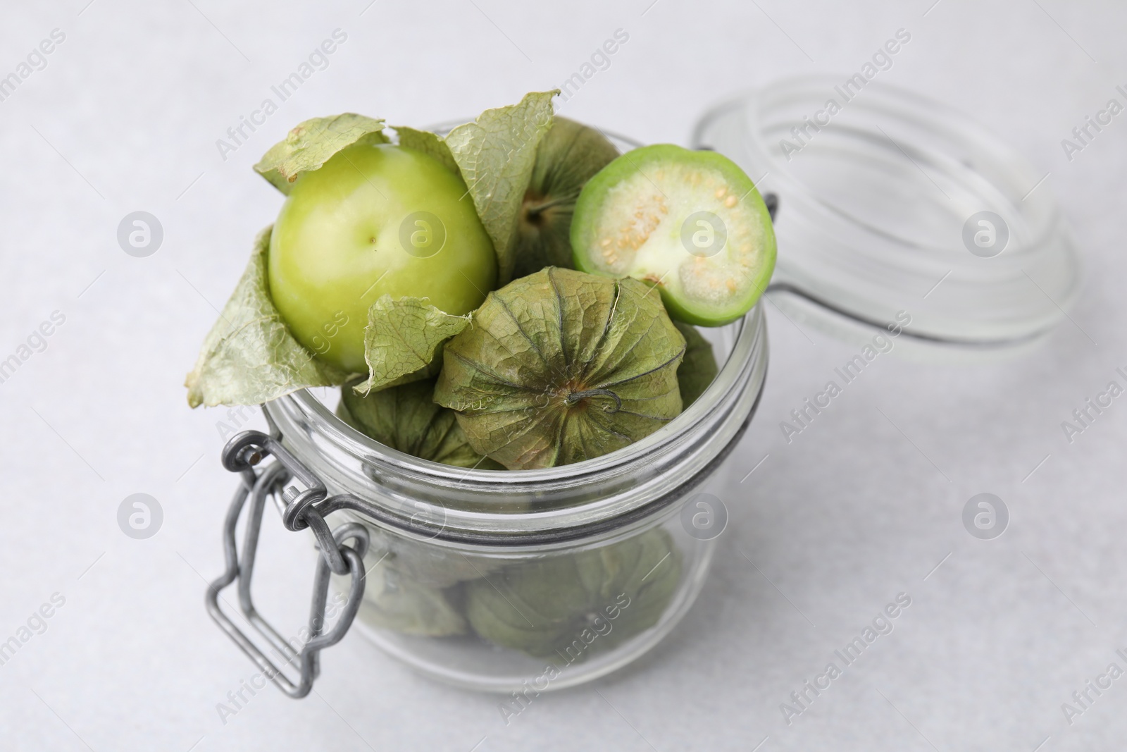 Photo of Fresh green tomatillos with husk in glass jar on light table, closeup