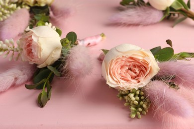Photo of Many small stylish boutonnieres on pink wooden table, closeup