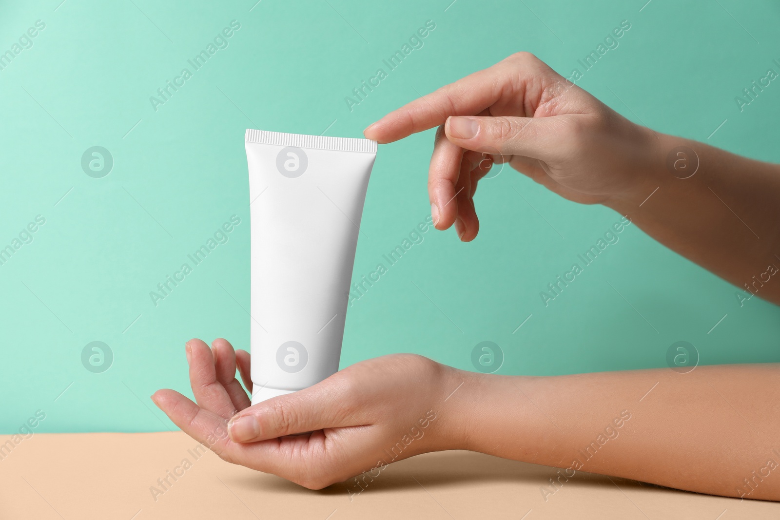 Photo of Tube of hand cream on beige table against turquoise background, closeup